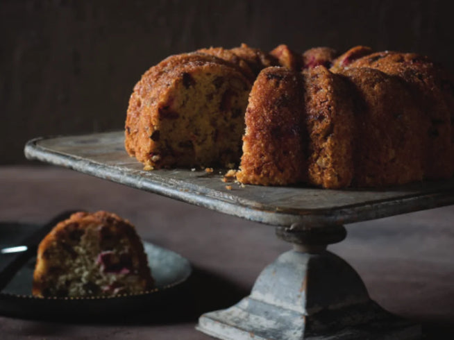 Cranberry bundt cake with a sugary crust on a weathered metal cake stand, with a slice served on a plate.