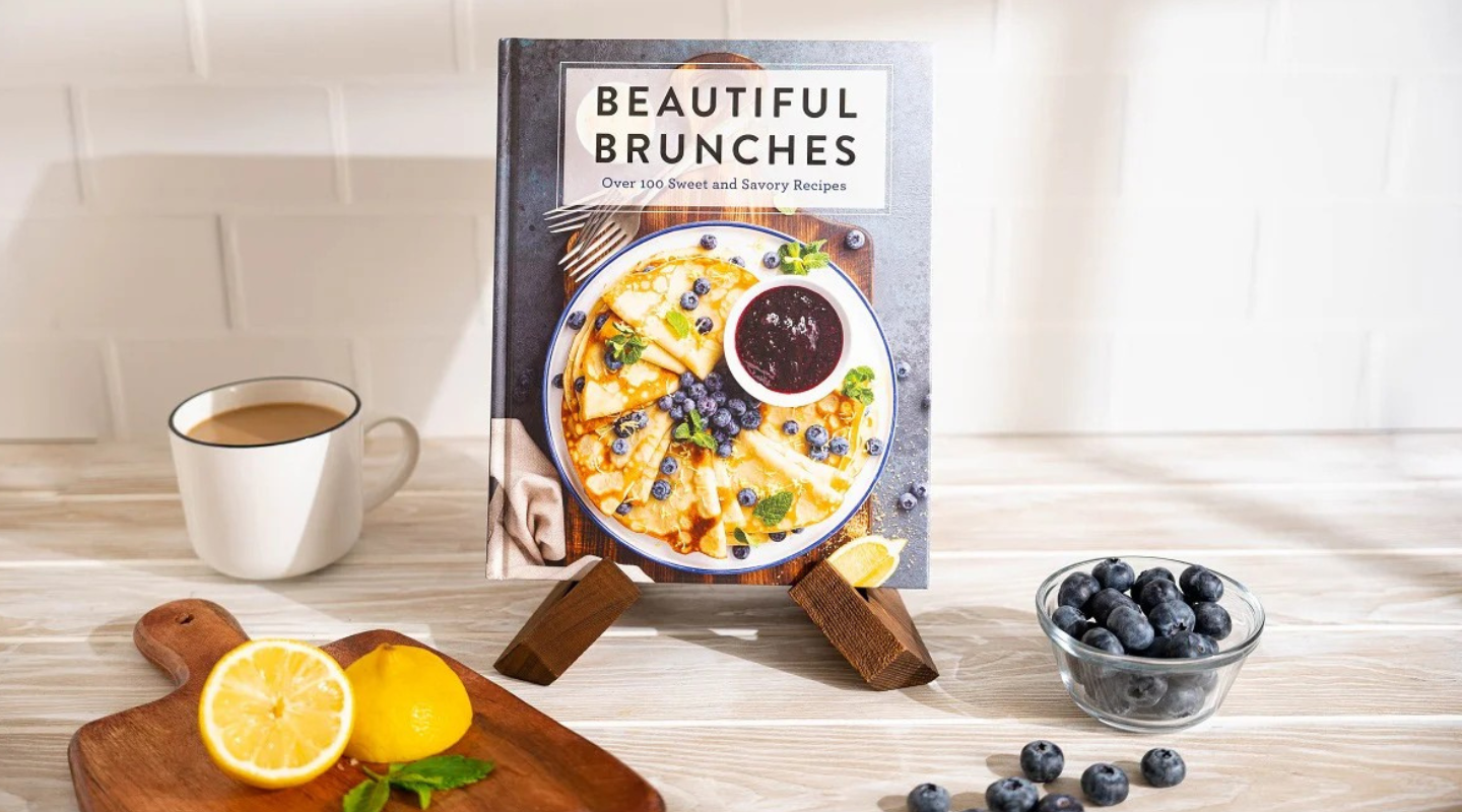 Cookbook titled 'Beautiful Brunches' on a stand with a cup of coffee, lemons, and blueberries on a wooden surface.