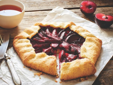 Plum galette on a wooden table with plums and a bowl of jam.